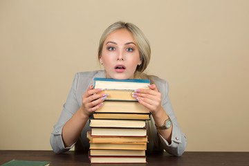 beautiful young woman in a suit sits at a table with books with a surprised face