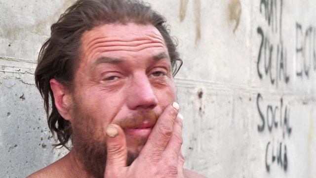 Down-and-out person on the street. Homeless man looks at the camera and talks. Real person with no fixed abode