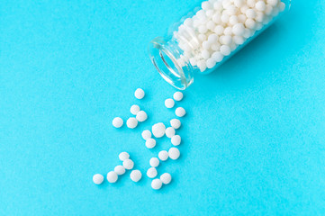 Homeopathic globules in glass bottle on pastel blue background. The globules are scattered from bottle. Alternative homeopathy medicine herbs, healthcare and pills concept. Selective focus