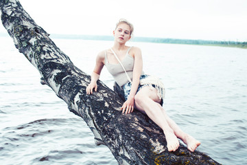 young blond woman hanging on birch tree at lake shore, summer vacations outdoor lifestyle