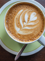 Close up white coffee cup with shape latte art foam on wood table.