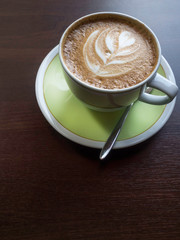 Close up white coffee cup with shape latte art foam on wood table.