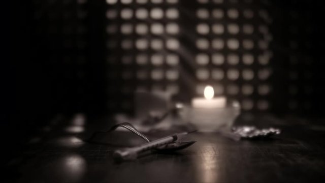 JUNKIE'S SYRINGE FALLS INTO FRAME AND SETTLES ON TOP OF A DIRTY SPOON.  NO PEOPLE.  BLACK AND WHITE.  SLOW MOTION AT 180 FPS.