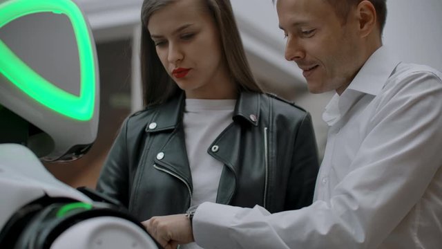 A man and a woman in the Mall interact with a robot consultant by tapping the screen and smiling. Cyborg Android helps people.