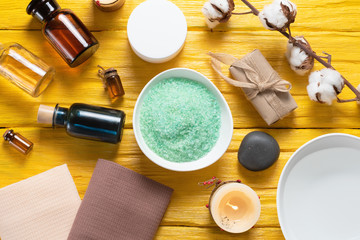 Spa flat lay concept background. Bath salt, aroma oil bottle, soap, towel and a water in bowl on a yellow background.