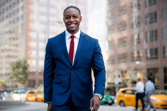 African american business professional in a suit and tie, smiling while walking to workplace office in financial district, city background