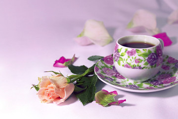 Morning. Pink rose flowers and porcelain cup of black coffee on the table. Pink and lilac tinted.
