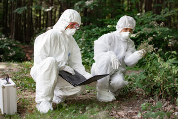 Ecological problem. Pollution. Examine soil. Scientist working in forest in protective mask and...