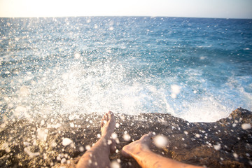 Fototapeta na wymiar man's feet chilling on a cliff in-front of the sea and water splashing 