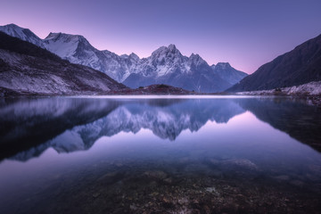Fototapeta na wymiar Mountain lake with perfect reflection at sunrise. Beautiful landscape with purple sky, snowy mountains, hills, fog over the lake at twilight in Nepal. Snow covered rocks is reflected in water. Nature