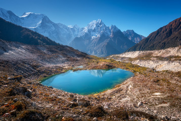 Fototapeta na wymiar Small lake with blue water and sky reflection against beautiful snow covered mountains at sunny day in autumn. Landscape with lake, snowy rocks, hills, stones at sunrise. Himalayan mountains in Nepal