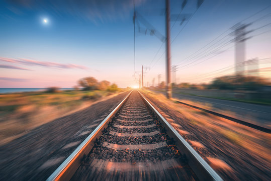Railroad and beautiful blue sky with full moon at sunset with motion blur effect in summer. Industrial landscape with railway station and blurred background.  Railway platform in speed motion. Concept