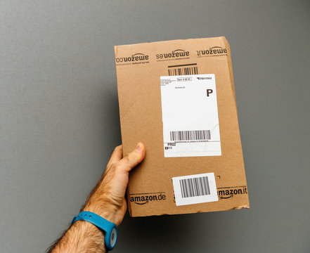 PARIS, FRANCE - OCT 30, 2017: Man Holding Amazon Germany Hermes Prime Cardboard Delivery Box Against Gray Background