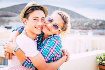 Obraz premium beautiful couple of mum and son together hugged in the terrace of the home having fun and laughing - woman with sunglasses and teenager with a relationship - guy with a hat hapy and funny