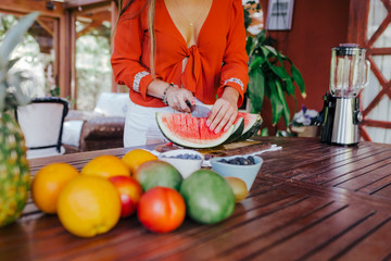 young woman preparing a healthy recipe of diverse fruits, watermelon, orange and blackberries. Using a mixer. Homemade, indoors, healthy lifestyle