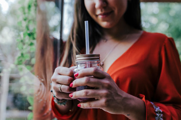 young beautiful woman standing by the window holding a healthy jug of smoothie. Home, indoors and lifestyle