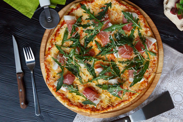 Pizza with bacon, cheese and herbs on a wooden dish on a black wooden background