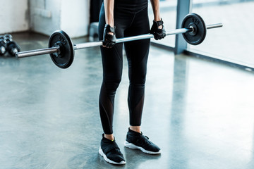 cropped view of young woman in sportswear working out with barbell in gym