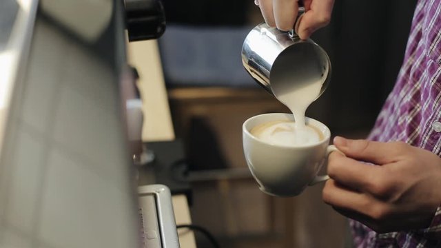 A close view of male bartender hands pouring steamed milk into a cup with espresso making latte