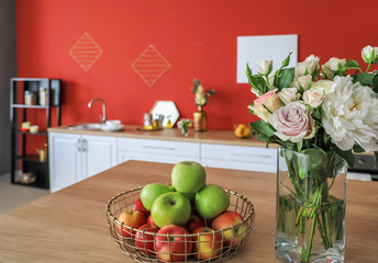Fresh apples on counter with bouquet of flowers on table in kitchen