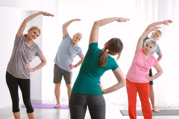 Fotobehang Senior people with young trainer doing exercises in nursing home © Pixel-Shot