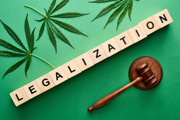 top view of green cannabis leaves and legalization word on wooden blocks near gavel on green...
