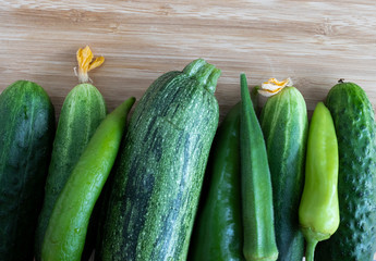 Cucumbers, hot peppers, green zucchini, green peppers on a light brown background, top view