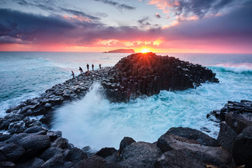 Fisherman on Giants Causeway at sunrise with red ball of the sun and nice clouds