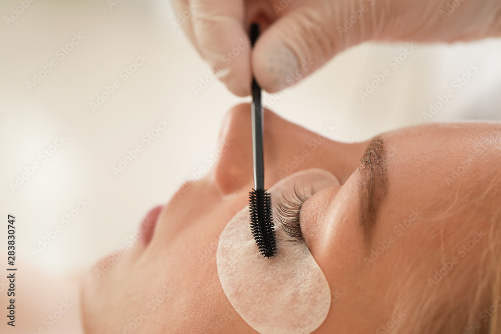 Wall mural young woman undergoing procedure of eyelashes lamination in beauty salon, closeup