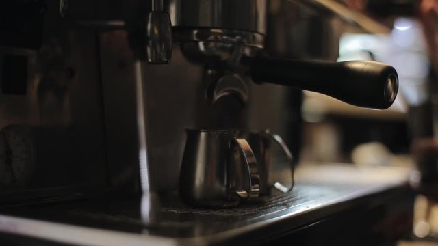 A close-up of espresso pouring from a professional coffee machine into two steel pitches
