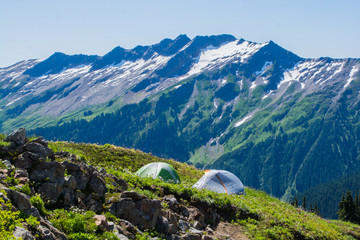 Fototapeta na wymiar tents on meadow hillside below rocky mountain range Glacier Peak Wilderness