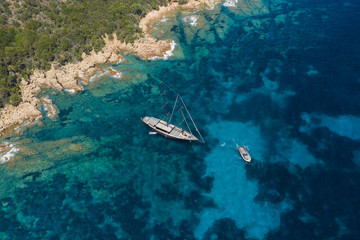 View from above, stunning aerial view of a luxury sailboat floating on a beautiful turquoise sea that bathes the green and rocky coasts of Sardinia. Emerald Coast (Costa Smeralda) Italy