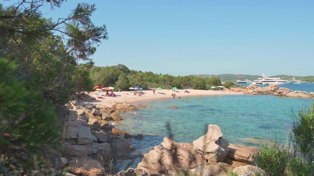 Stunning view of a beautiful beach with tourists sunbathing and swimming on a turquoise clear sea, Emerald coast  Sardinia, Italy.
