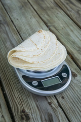 Low carb tortillas on a scale on wooden background - room for copy space.