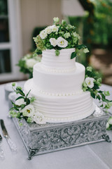 bride and groom cutting white wedding cake with green and white flowers, three tiered cake, silver...
