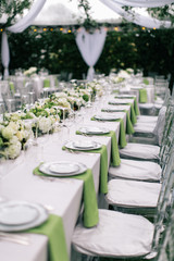 wedding reception table setting, fine china plates, green napkin hanging off table, silverware, wine glasses, and flower arrangments