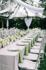 Outdoor summer wedding tent decorated with hanging fabric, greenery, and crystal chandeliers, wedding reception tables, green accent color