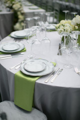 wedding reception table setting, fine china plates, green napkin hanging off table, silverware, wine glasses, and flower arrangments