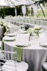 wedding reception table setting, fine china plates, green napkin hanging off table, silverware, wine glasses, and flower arrangments