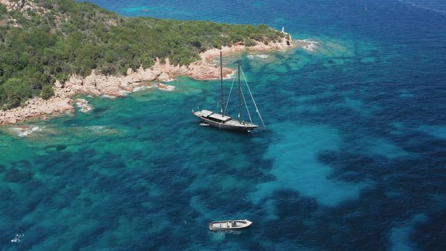 View from above, stunning aerial view of a luxury sailboat floating on a beautiful turquoise clear sea that bathes the green and rocky coasts of Sardinia. Emerald Coast  Italy.