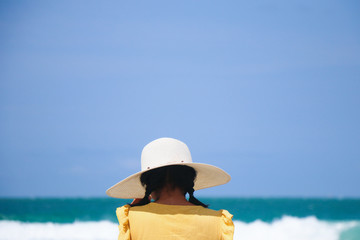 Back of woman on the beach wearing white hat protect UV in sunny day