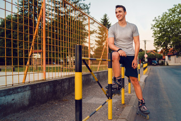 Young man on roller blades skates sitting on the fence wall looking waiting in a summer day evening rollerblade