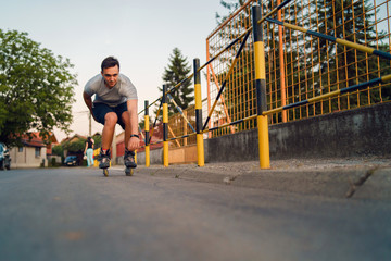 Young man on roller blades skates riding by the fence wall looking waiting in a summer day evening...