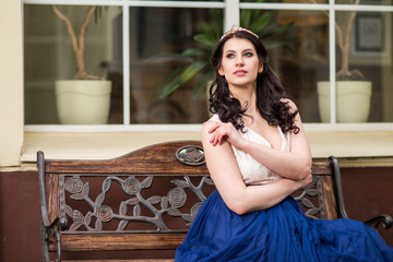 Portrait of Beautiful Sensual Young Female With Tiara Posing On Bench in City