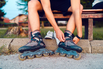 Close up on legs of man putting his roller blade skates on the feet while sitting on the bench in a...
