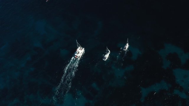 View from above, stunning aerial view of a catamaran and two sailboats sailing on a blue sea. Emerald Coast  Sardinia, Italy.