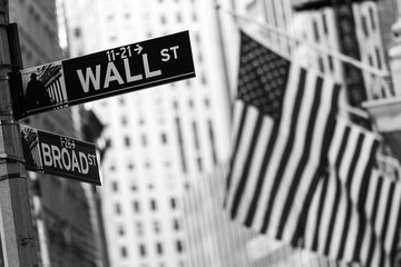 Wall street sign in New York City with American flags and New York Stock Exchange in background. Black and white image. © kasto