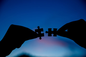 two hands trying to connect couple puzzle piece with sunset background.
