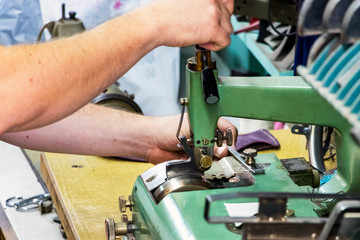 Male shoemaker hands skiving leather with a vintage skiving machine.