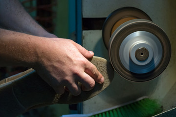 Fototapeta premium Male shoemaker hands grinding and shaping a sole in his workshop, close up.